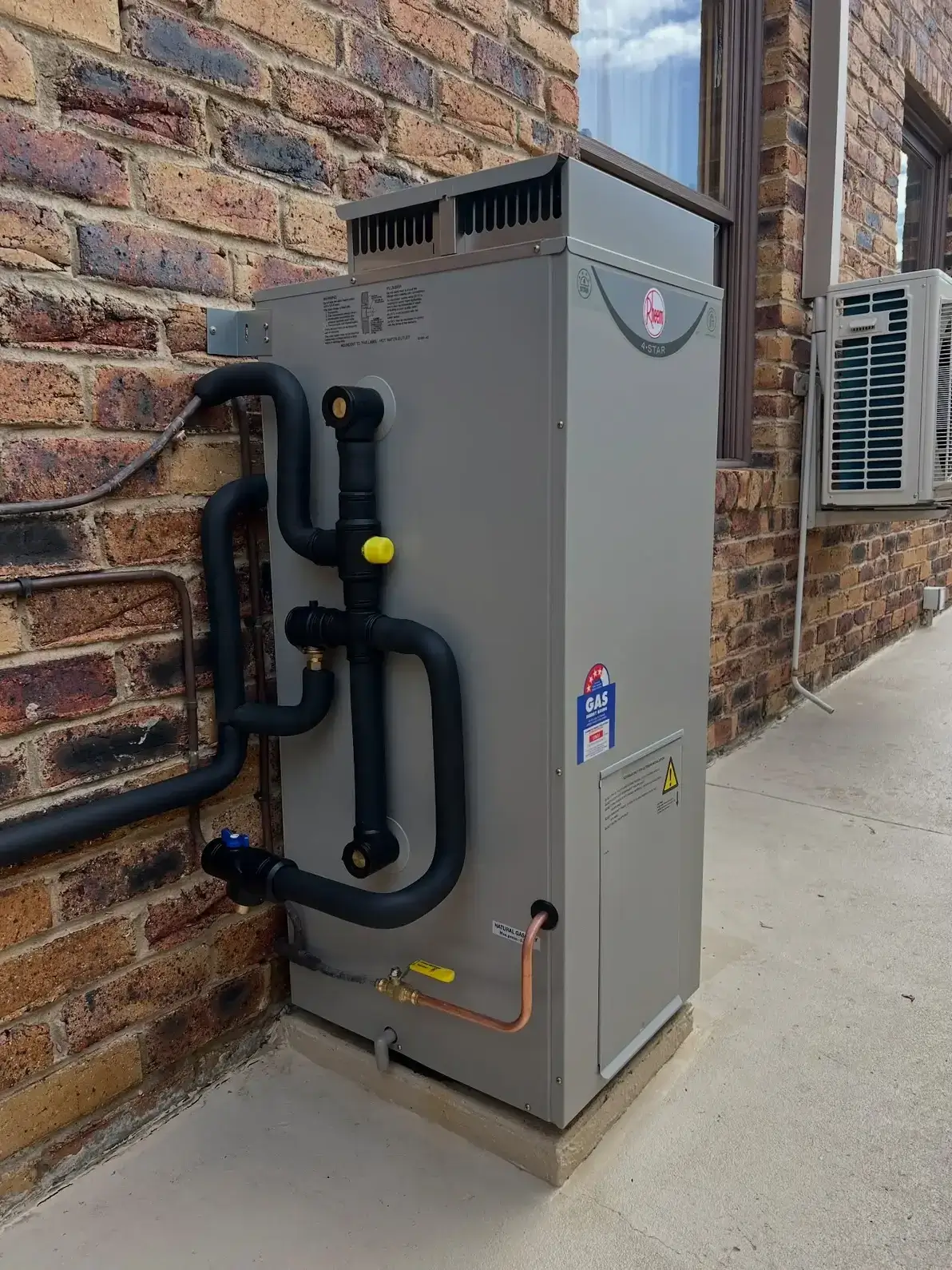 Rheem 4-Star natural gas storage hot water system installed against a brick wall on a concrete pad at a Brisbane home